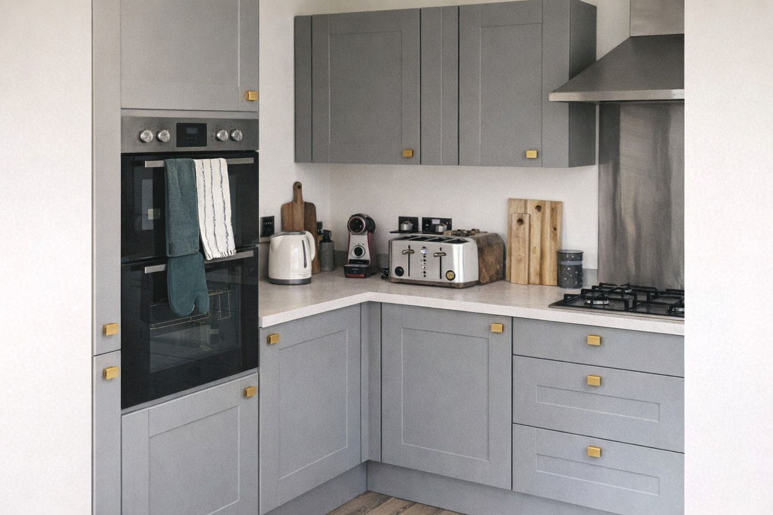 Grijze keuken met kleine goudkleurige vierkante handgrepen op kastjes en laden.